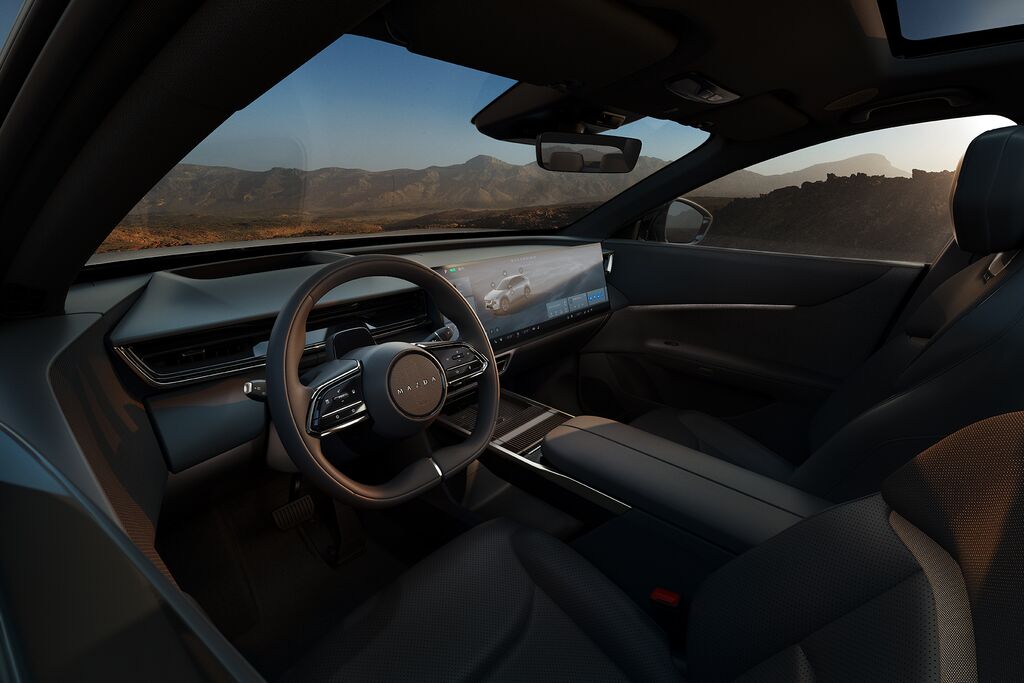 Interior of Mazda CX-6e electric SUV featuring a modern dashboard, panoramic digital display, and premium leather seats with a scenic mountain view through the windshield.