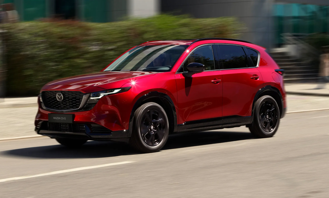 Third‑generation Mazda CX‑5 in red driving through an urban street, highlighting its modern design, sleek body lines, and dynamic motion.