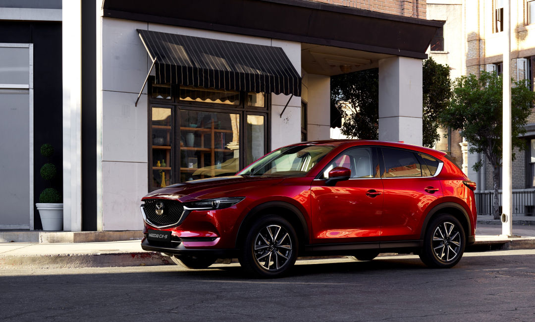 Second‑generation Mazda CX‑5 in red parked on a city street, highlighting its sleek profile and refined Kodo design.