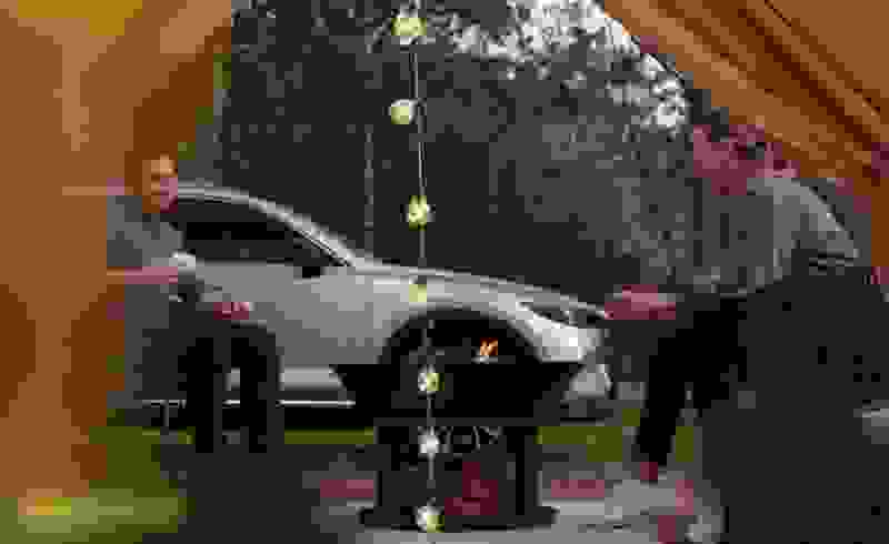 A couple sitting by a campfire outside a tent, enjoying the warmth and coziness of the moment with the reassurance provided by Mazda Assured.