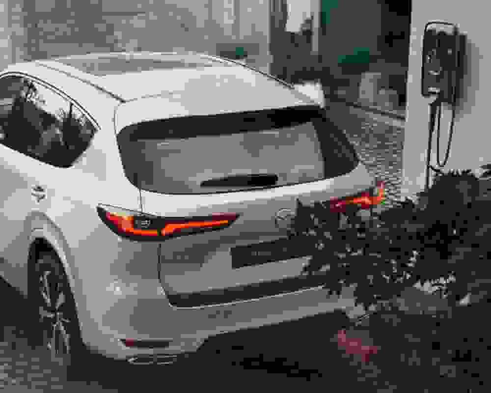 A Mazda CX 60 plug in hybrid parked in front of a house, showcasing its sleek design with the assistance of Mazda Finance.