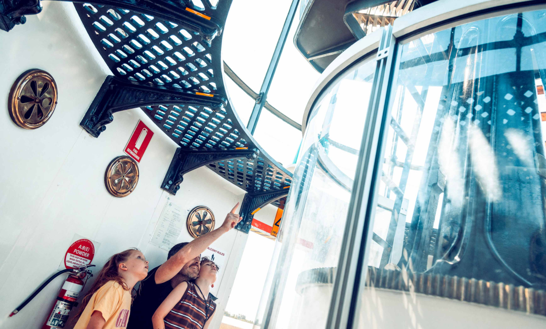 Family looking up at the historic 700-prism lens inside Norah Head Lighthouse