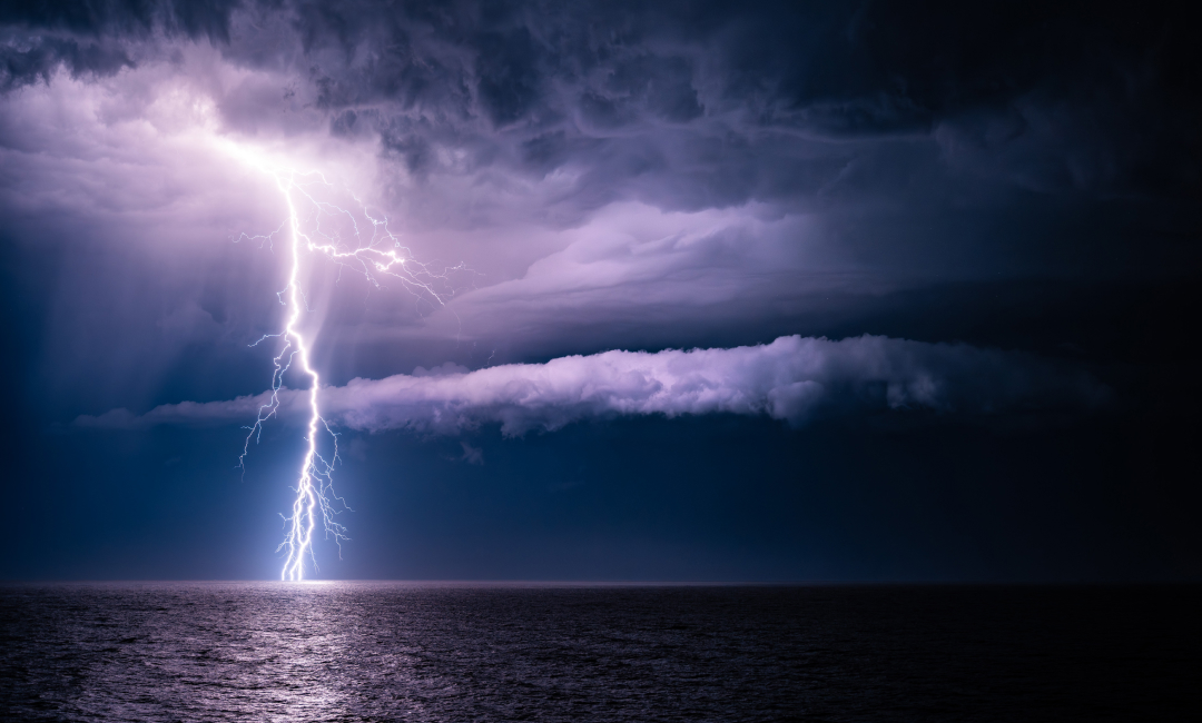 Lightning striking the ocean beneath towering storm clouds during a powerful night-time storm in Australia.