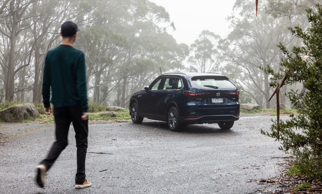 Mazda CX-80 Pure family SUV parked in misty Yarra Valley bushland, with driver approaching on a quiet forest road in Victoria, Australia