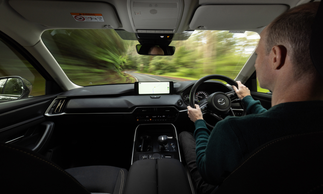 Interior driving view of Mazda CX-80 Pure family SUV on winding Yarra Valley road, with driver navigating through lush forest scenery