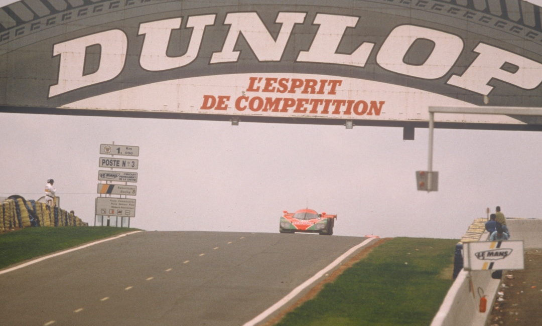 Mazda 787B No.55 racing under the Dunlop Bridge during the 1991 Le Mans 24 Hours, approaching the crest of the circuit
