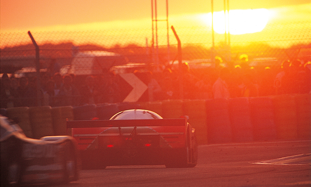 Mazda 787B No.55 silhouetted at sunset during the 1991 Le Mans 24 Hours, rear view of the iconic rotary-powered race car on track
