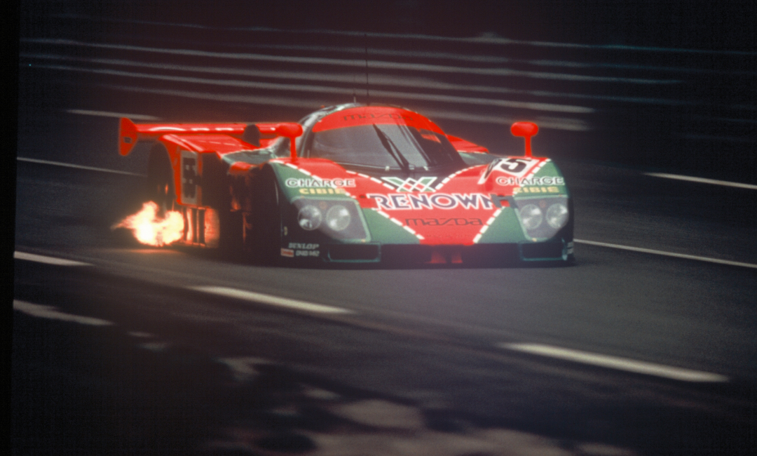 Mazda 787B No.55 in Renown livery racing at night during the 1991 Le Mans 24 Hours, with flames visible from the exhaust of the rotary-powered race car