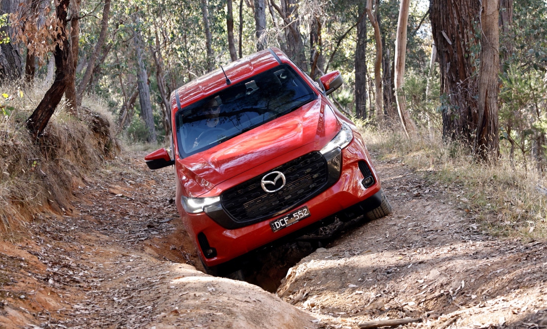 Red Mazda BT-50 GT four-wheel driving through ruts on a forest track
