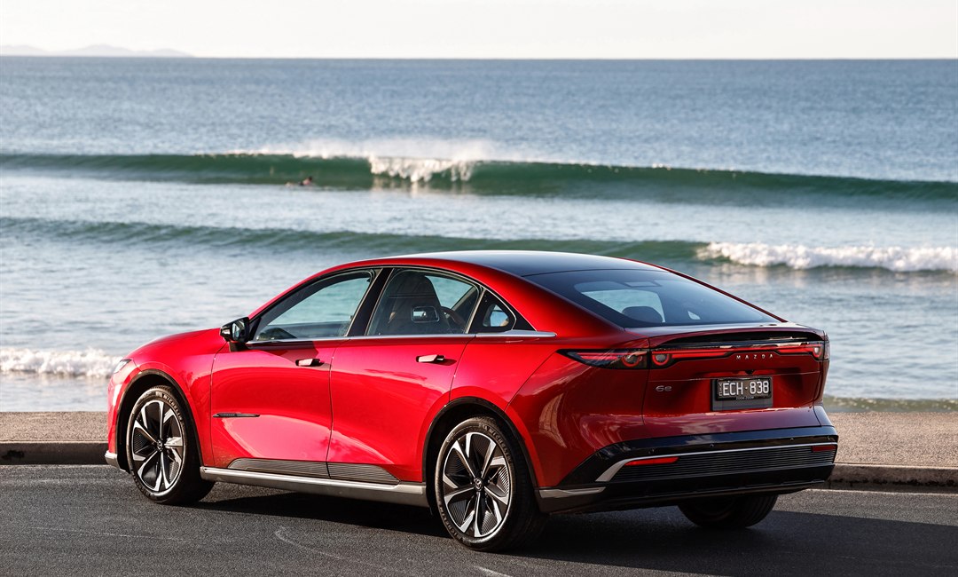 Rear three-quarter view of the Mazda 6e showing its full-width light bar, by the coast