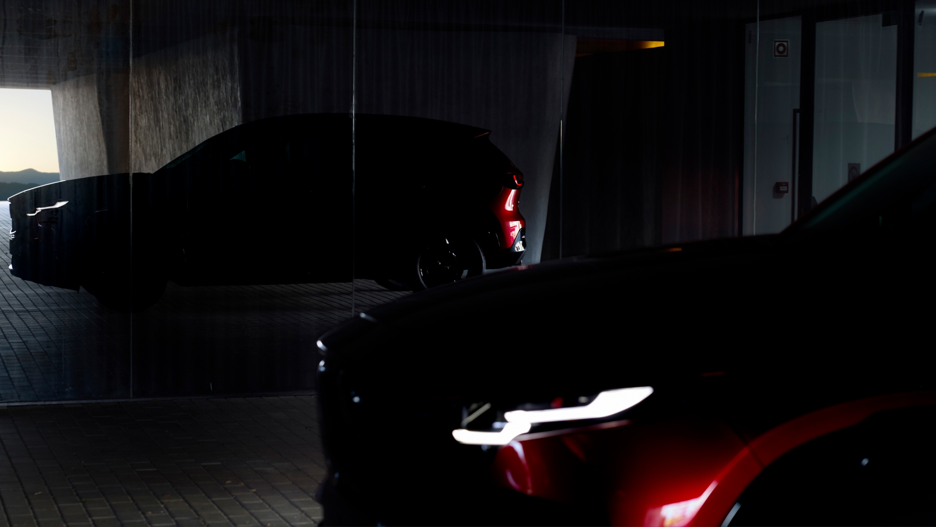 2026 Mazda CX-5 teaser showing sleek silhouette of red SUV under dramatic lighting—preview of next-generation design with bold styling and modern SUV proportions.