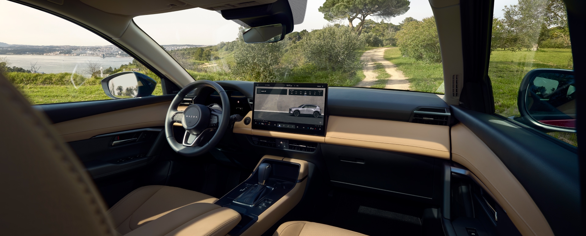 2026 Mazda CX-5 driver-focused interior with beige and black trim, large central touchscreen display, and scenic coastal view—modern SUV cockpit with advanced infotainment and premium design.