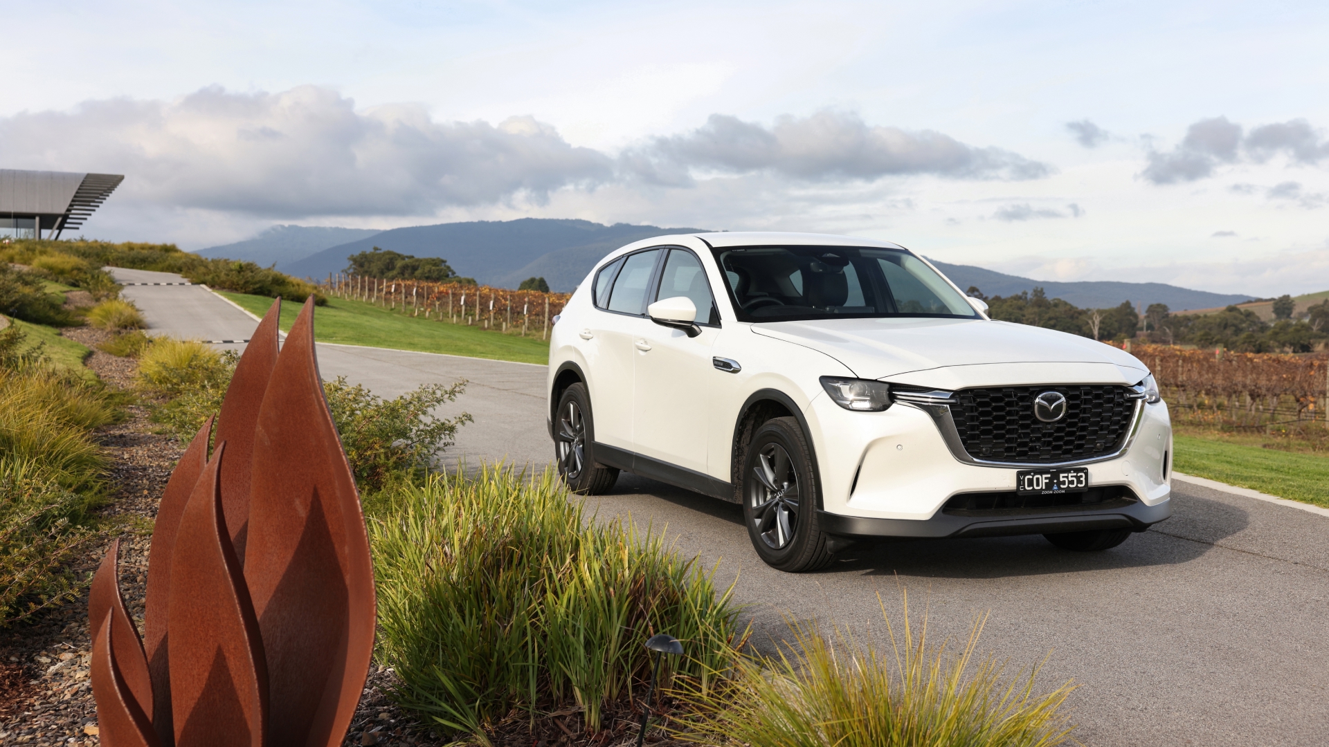Front three-quarter view of a white Mazda CX-60 PHEV driving along a scenic Australian coastal road.