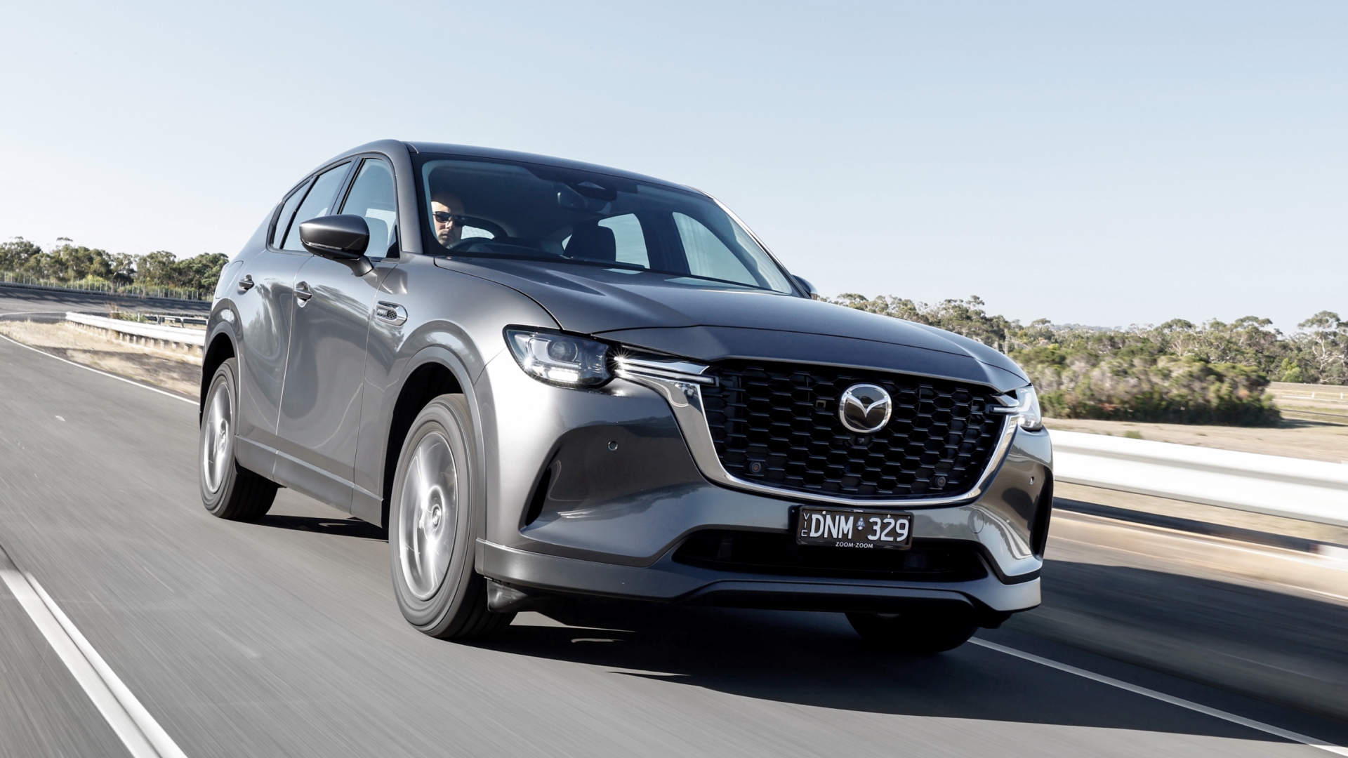 Mazda CX‑60 PHEV driving along a scenic road, highlighting its dynamic performance and elegant design in motion