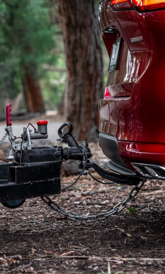 Close-up of Mazda trailer hitch connection with coupling mechanism, handle, and electrical connector—highlighting secure towing setup and integrated lighting system.