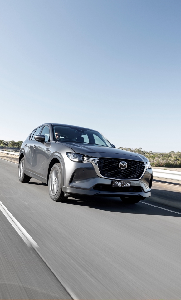 Mazda CX‑60 PHEV driving along a scenic road, highlighting its dynamic performance and elegant design in motion