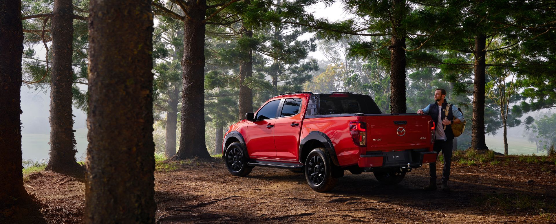 All-New 2025 Red Earth Mazda BT-50 ute parked in a tranquil forest with tall trees, showcasing rugged design and readiness for outdoor adventure.