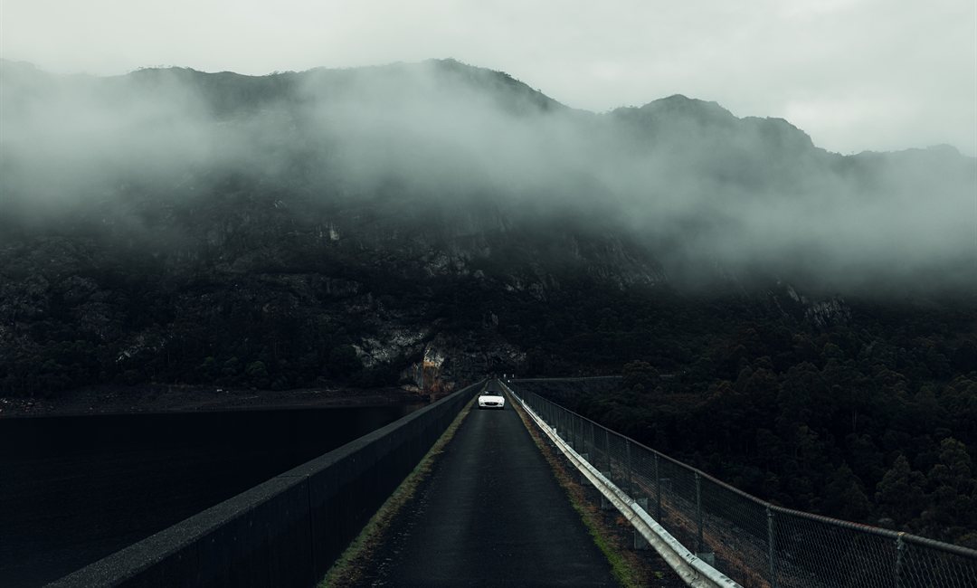 Mazda MX-5 crossing a dam causeway as fog rolls over the forested mountains of Tasmania's West Coast.