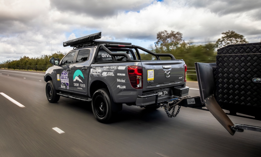 Grey Mazda BT-50 ute towing a trailer on the highway - promoting adventure travel and charitable road trips.