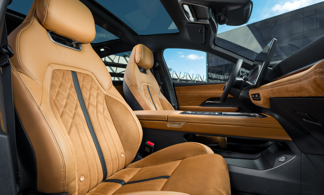 Luxurious tan leather front seats inside a Mazda 6 electric sedan, featuring diamond-quilted stitching, black accent stripes, and a modern dashboard with premium materials, photographed under natural light with a panoramic glass roof view.
