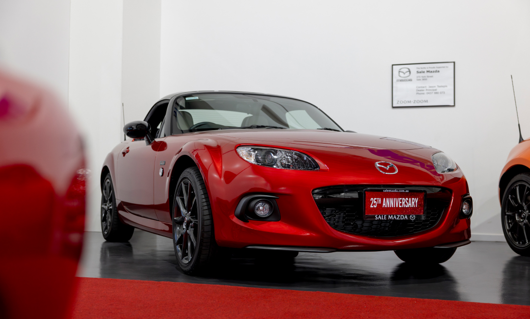 Mazda MX-5 25th Anniversary Edition in vibrant red displayed indoors on a red carpet, featuring sleek black alloy wheels and commemorative badging, part of Australia&rsquo;s greatest MX-5 collection.